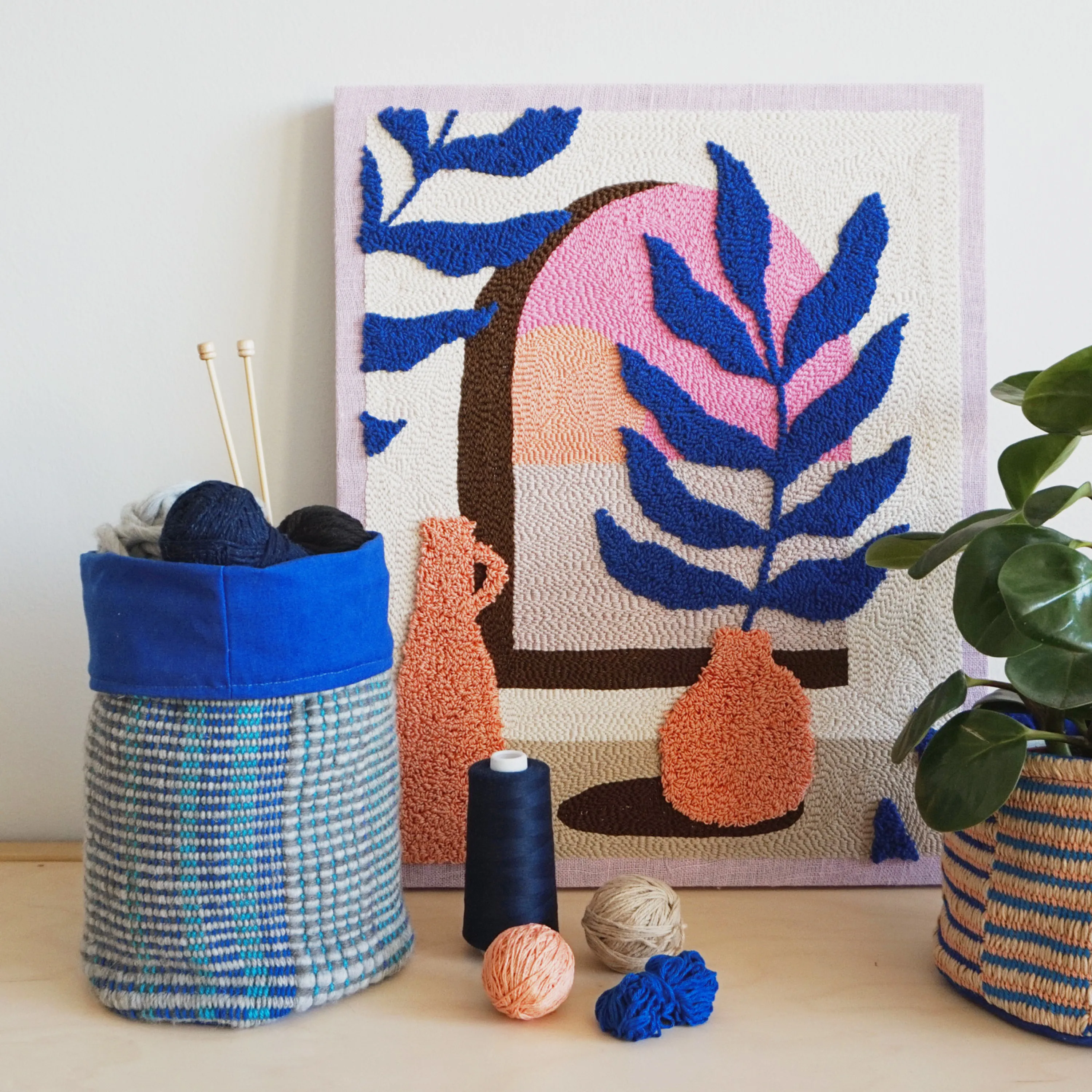 Textile artwork leaning on a wall and styled with a plant.
