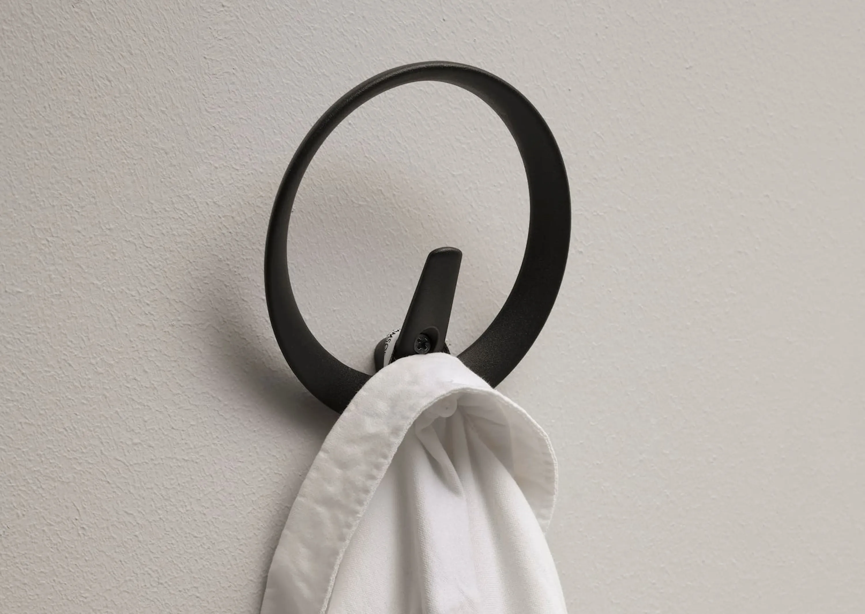 Black recycled aluminium wall hook holding a white shirt.