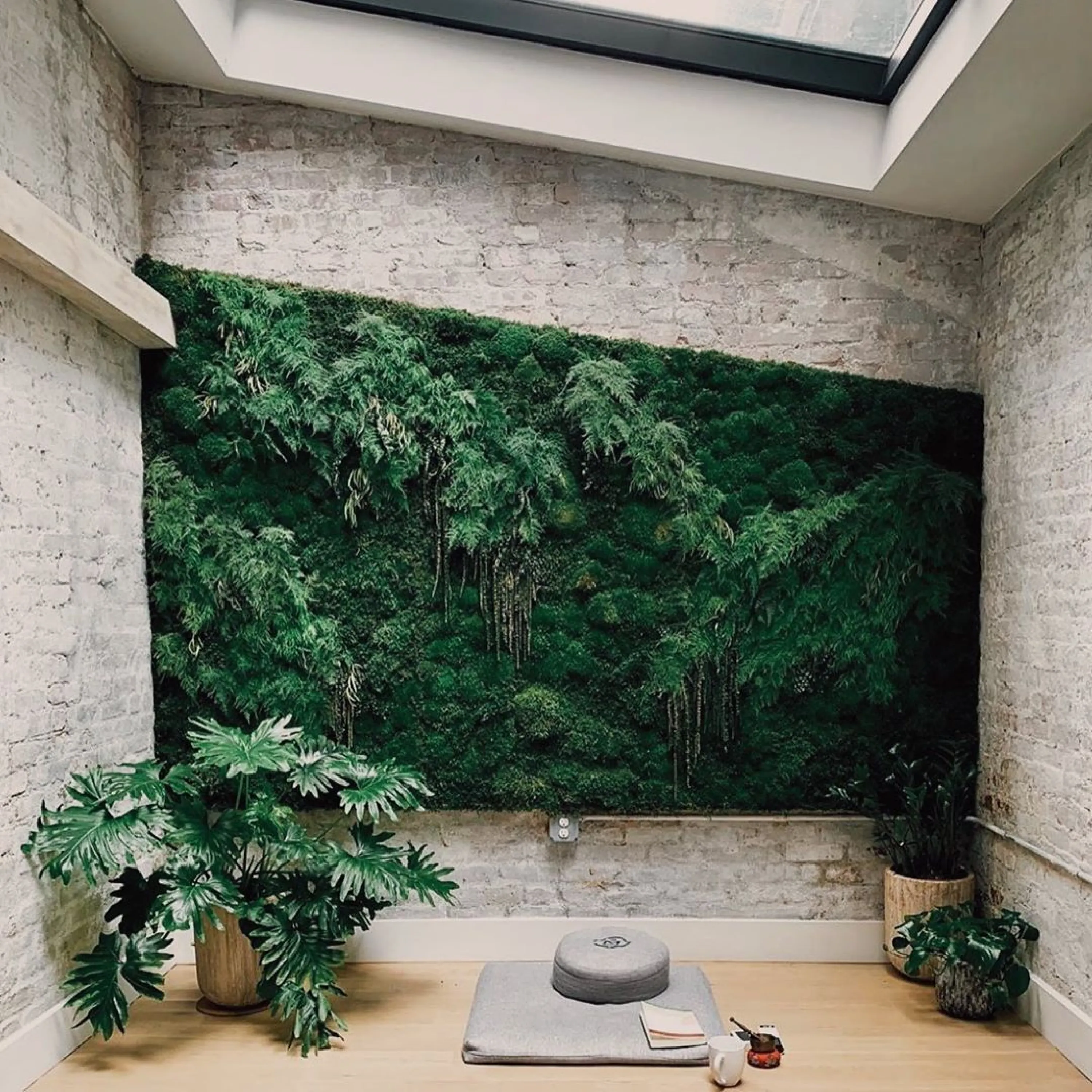 Meditation space on a room with a huge green wall and plenty of plants around.