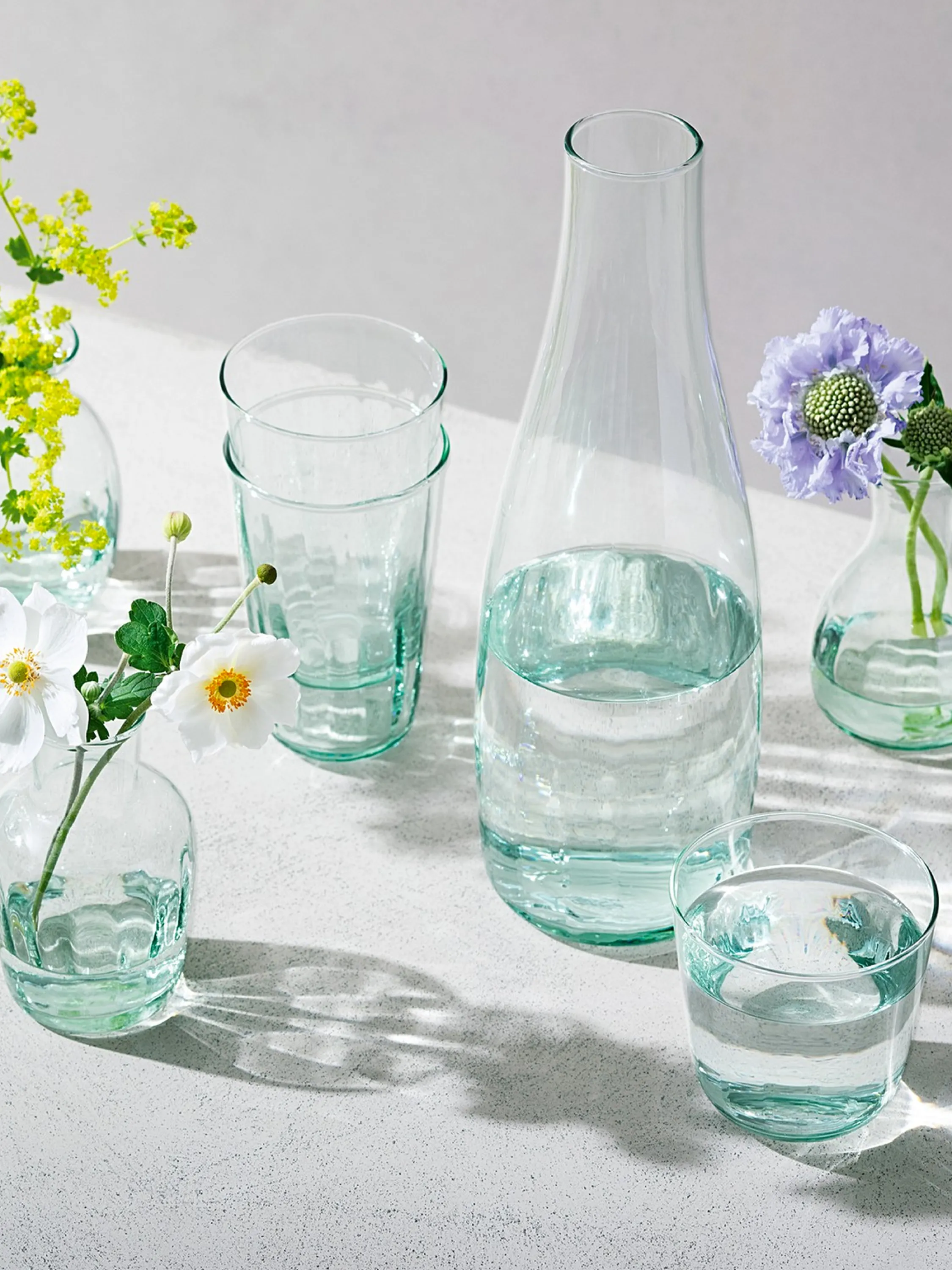 Recycled glass carafe and glasses styled on a table with flowers.