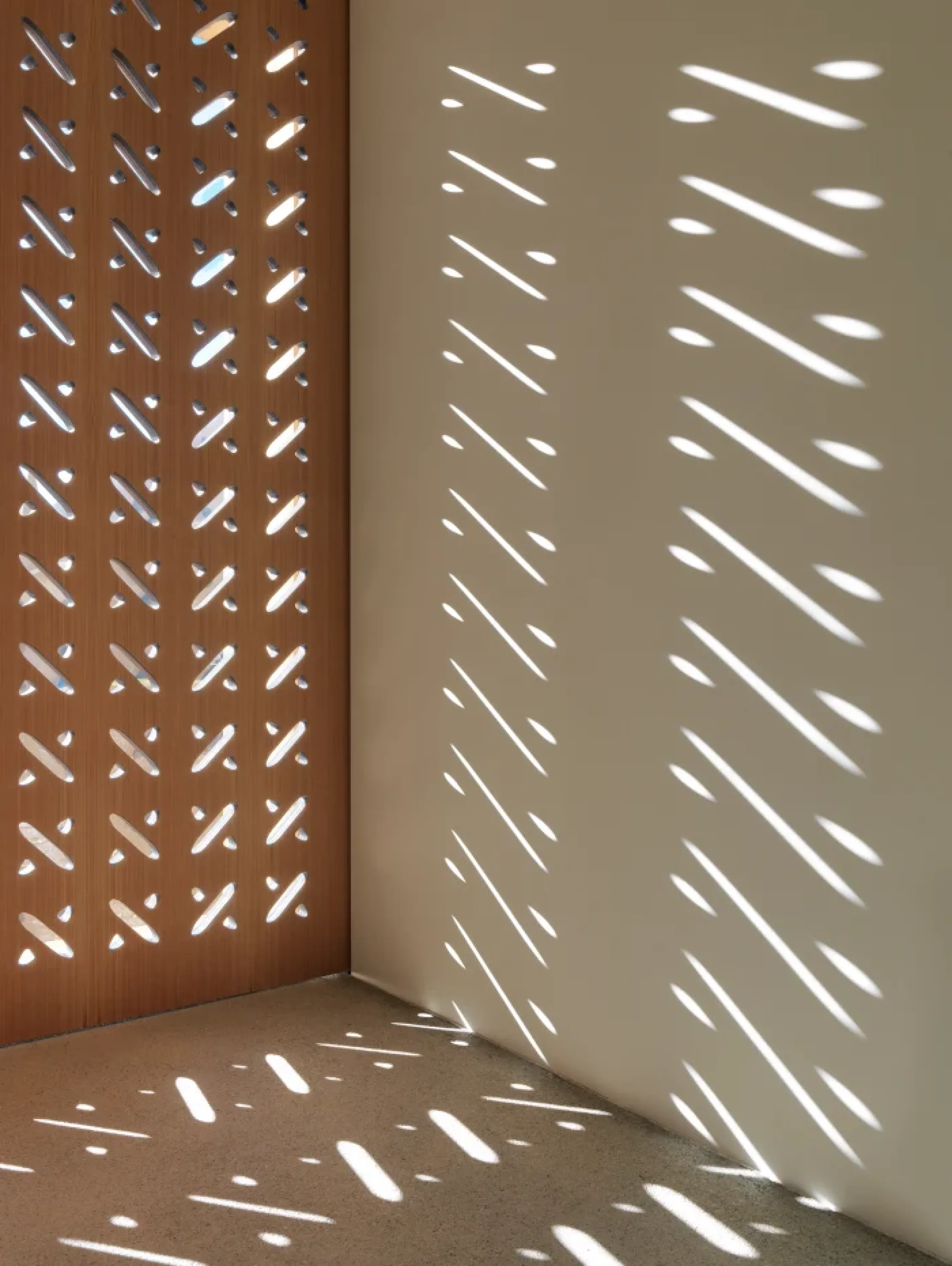 Perforated partition letting light draw shapes on the wall.