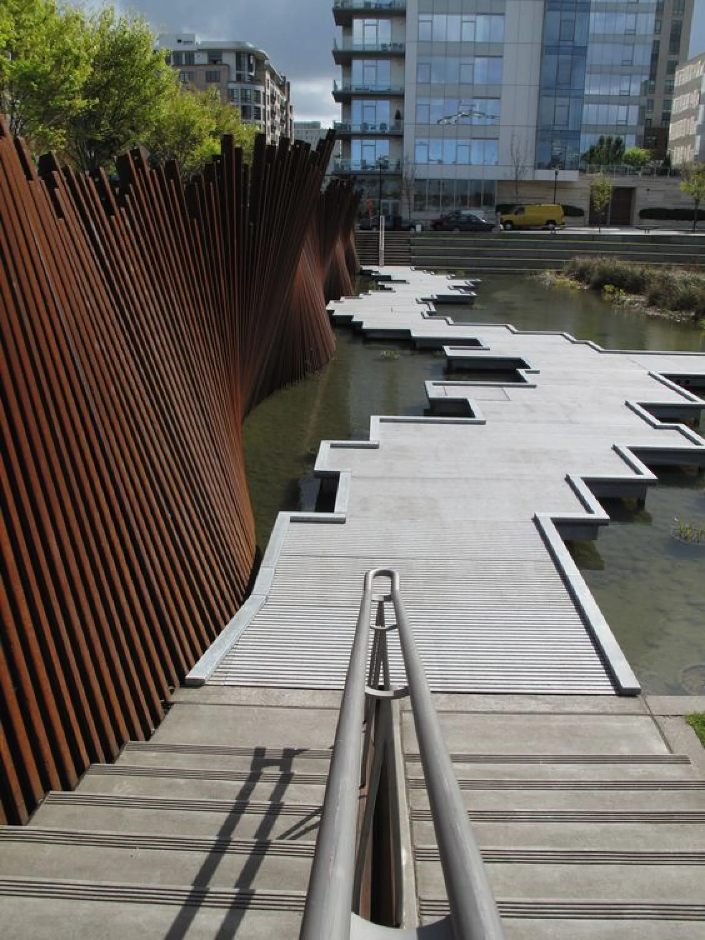 Public park enclosed with a wavy and partially see-through corten partition.