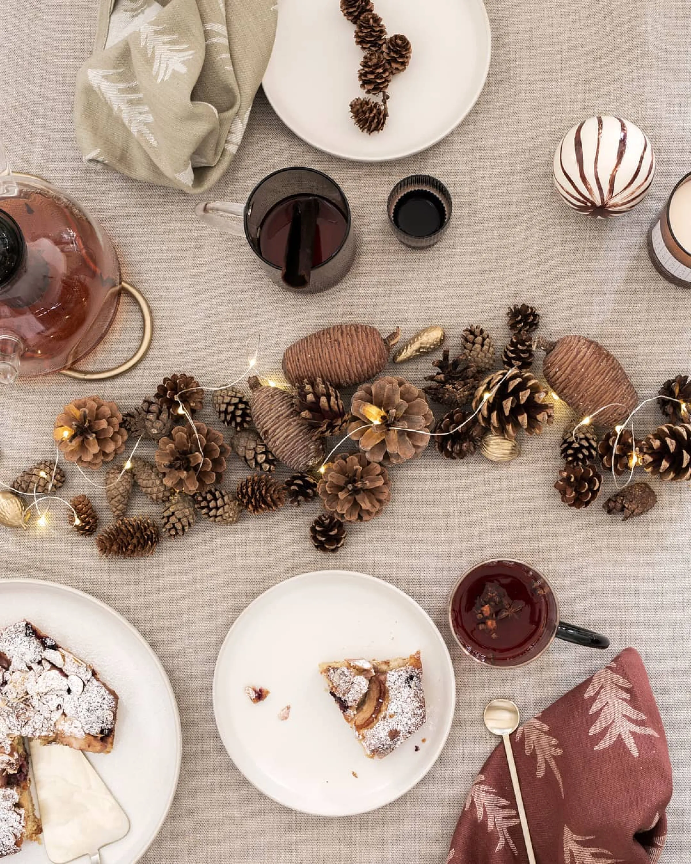 Top shot of a festive table setting with pinecones and string lights creating a sustainable Christmas centrepiece in the middle of the table.