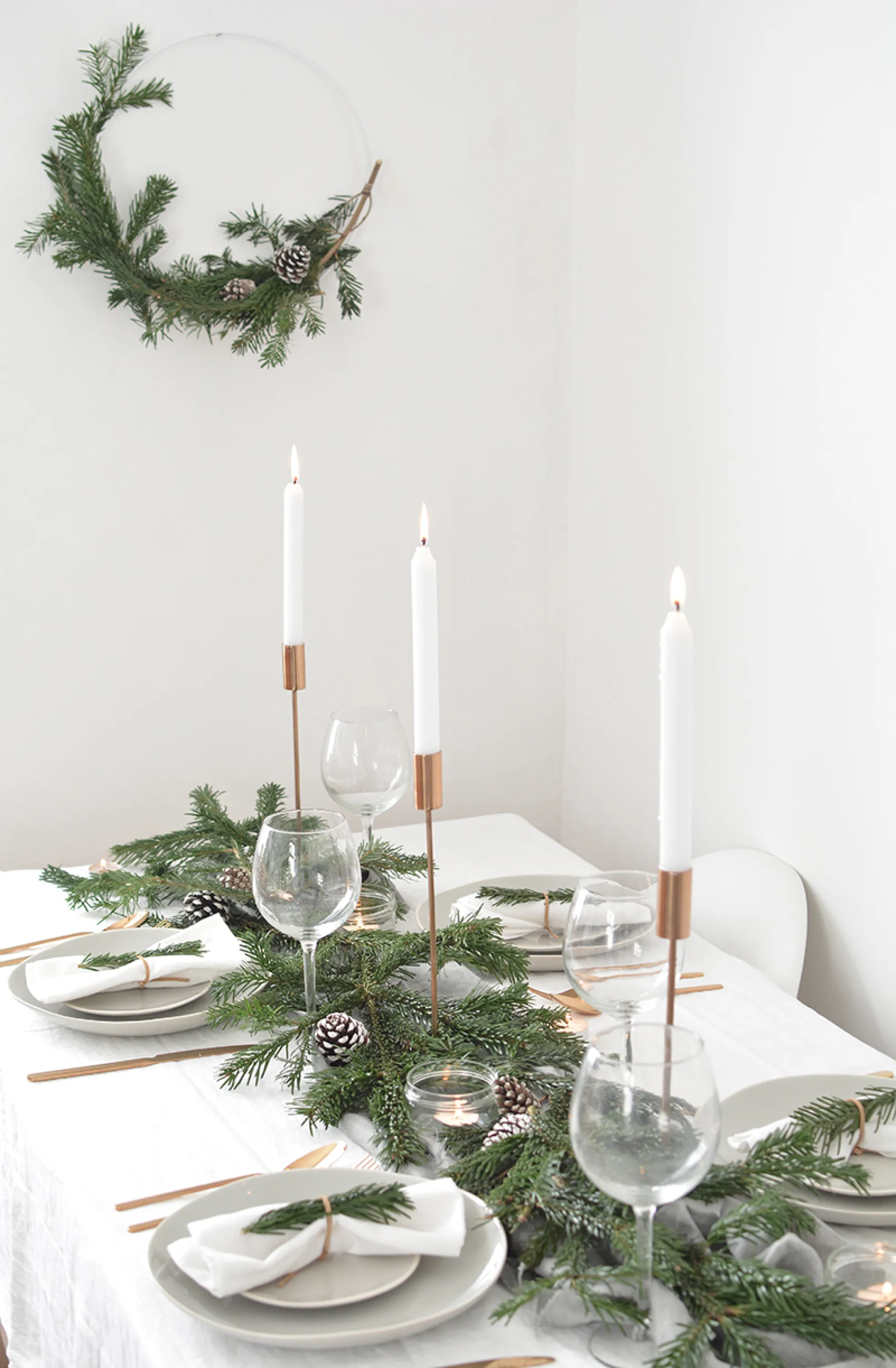 Total white festive table setting with greens and tall candles as a centrepiece.