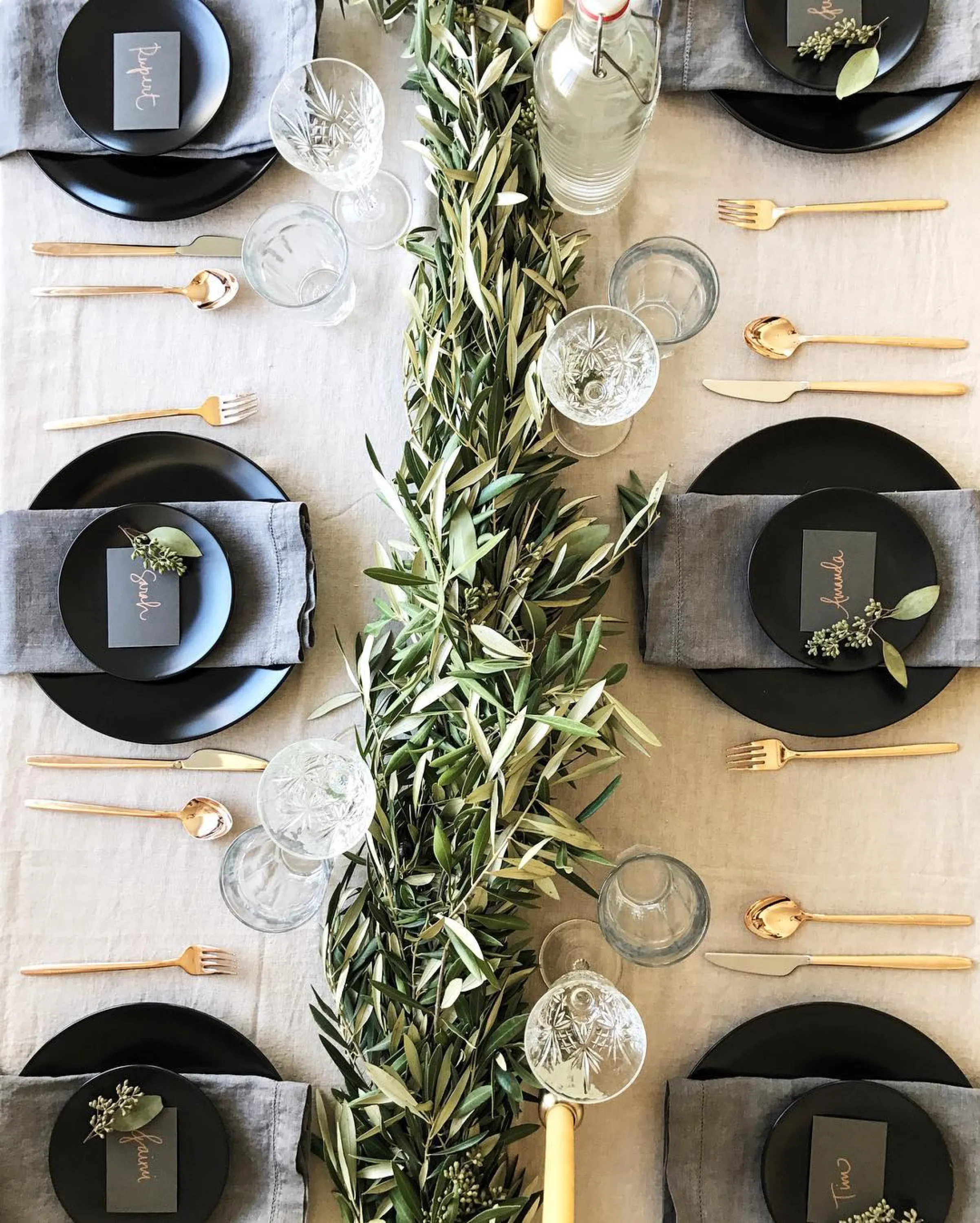 Black and gold table setting with olive branches as a centrepiece.