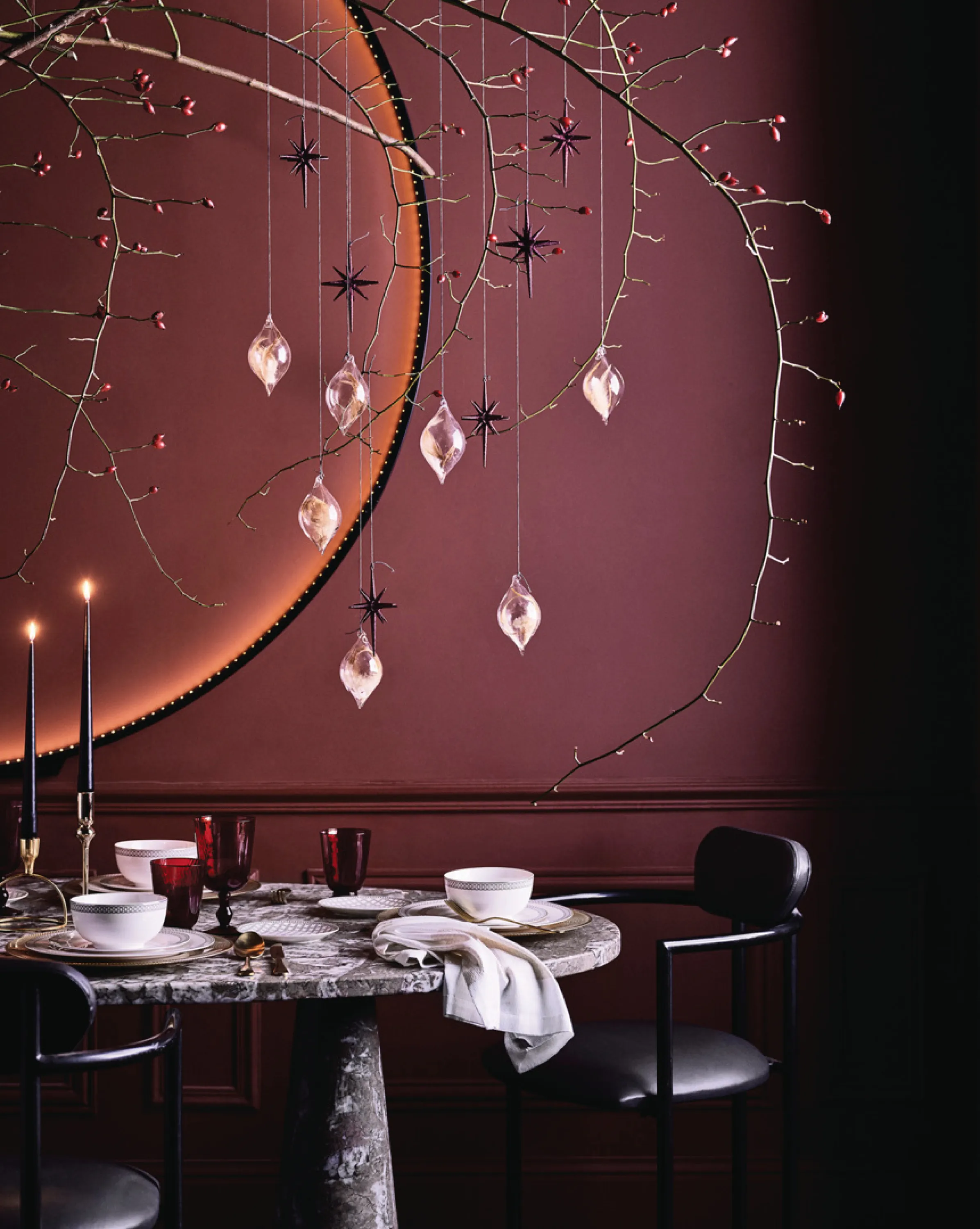 Branch with Christmas ornaments hung over a modern dining table.
