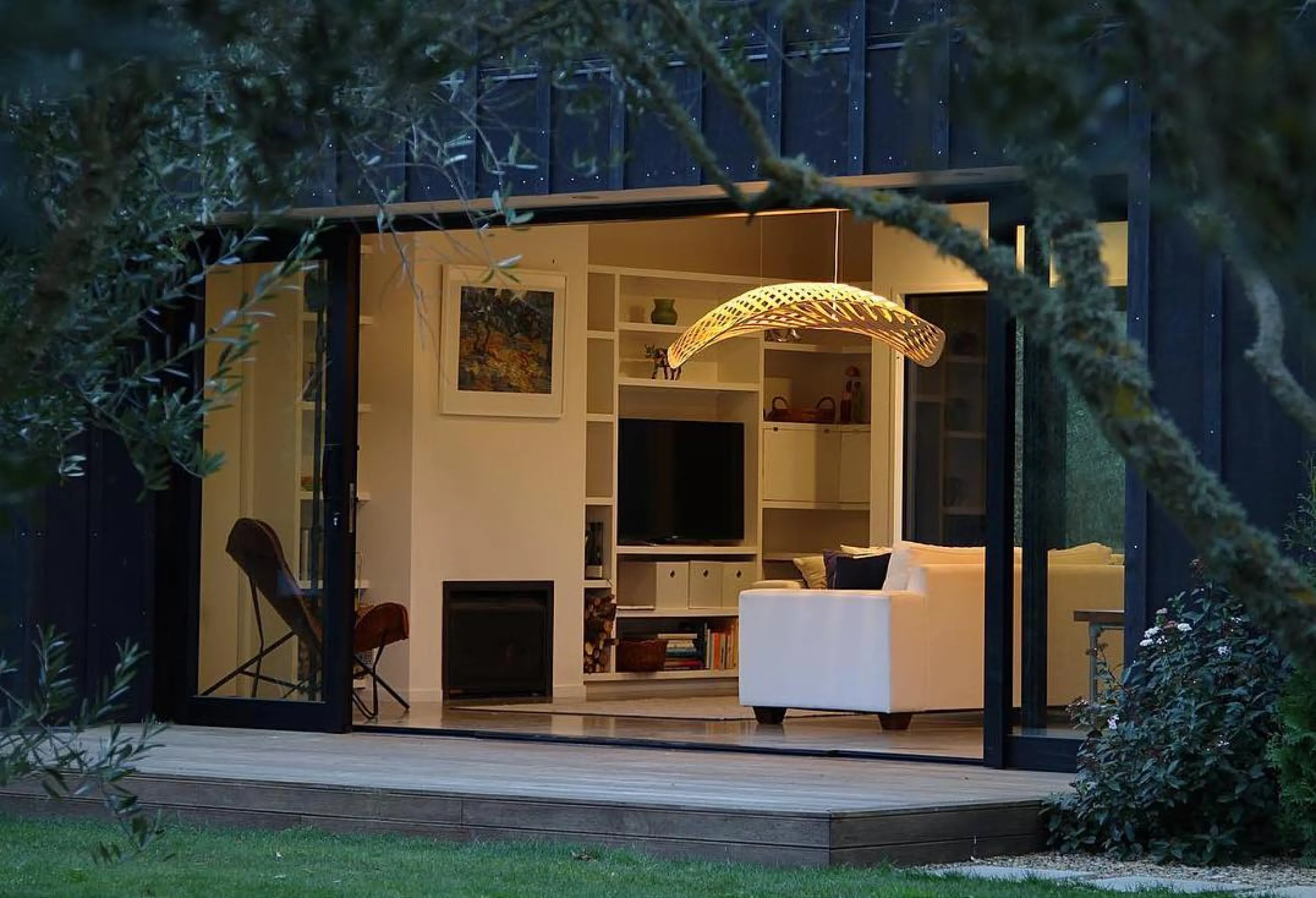 Shoot of a living room over branches highlighting a sinuous light fixture.