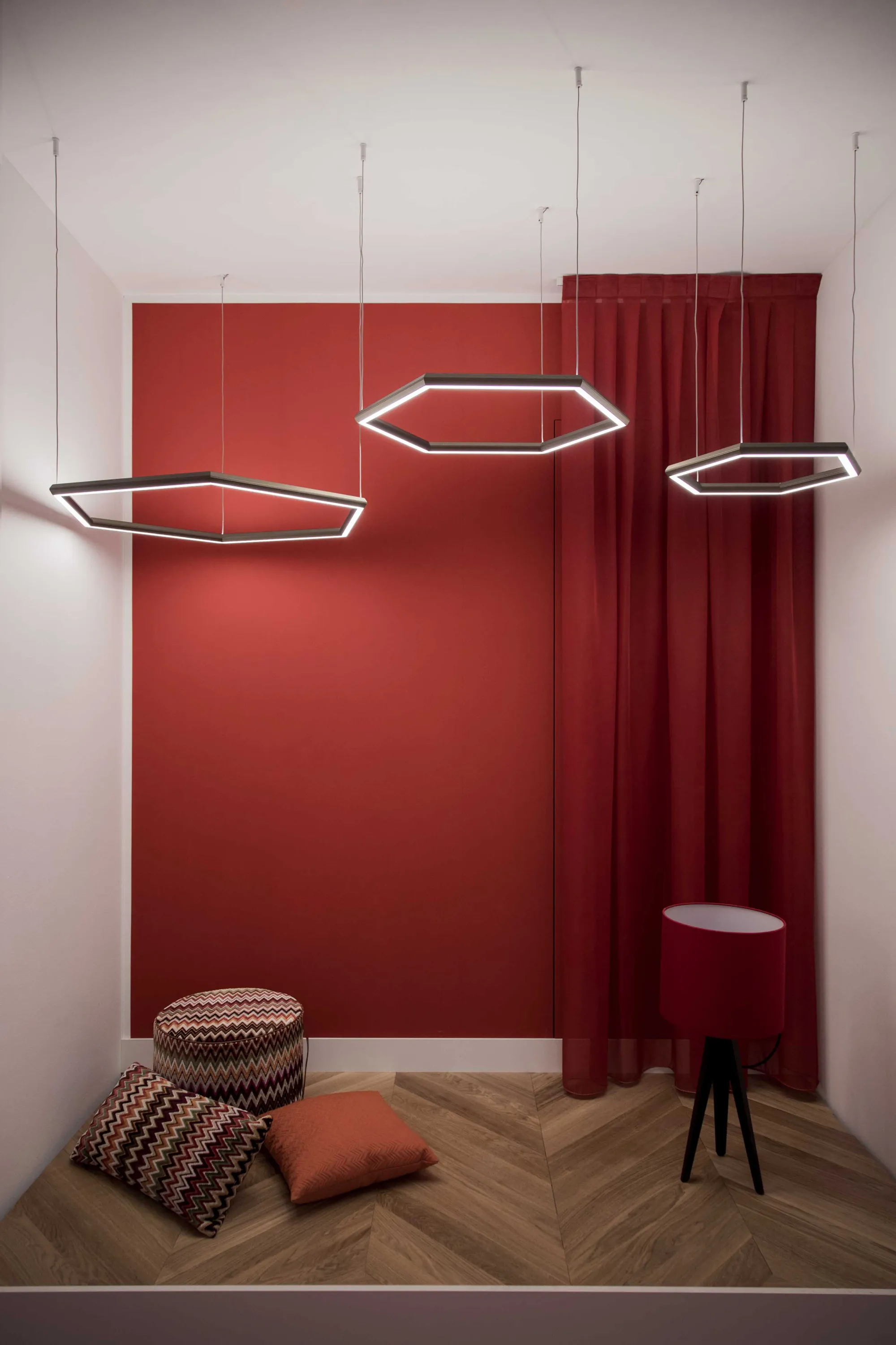 Hexagonal pendant lights hanging from the wall in a changing room with a focal back wall painted in red.