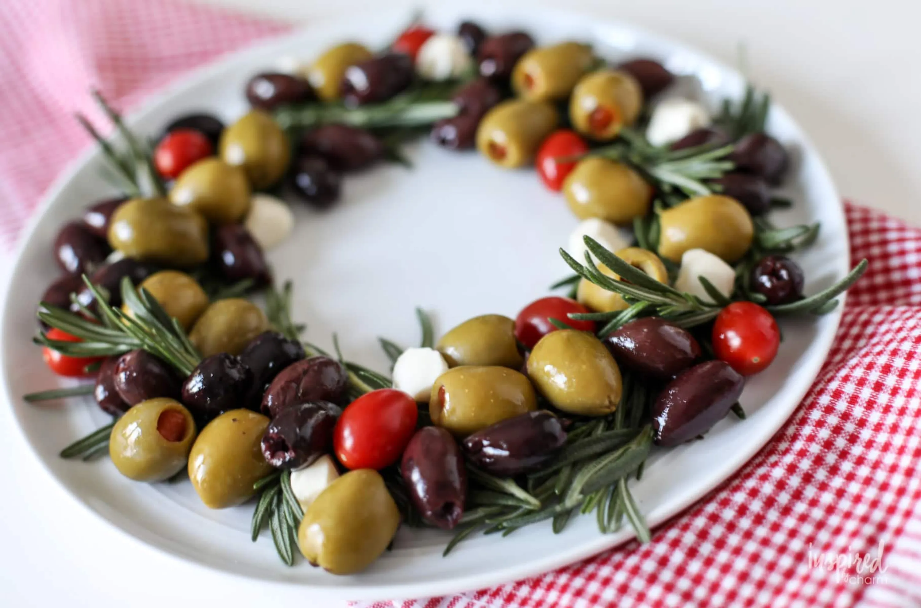 Rosemary and olives arranged in the shape of a wreath on a white plate.