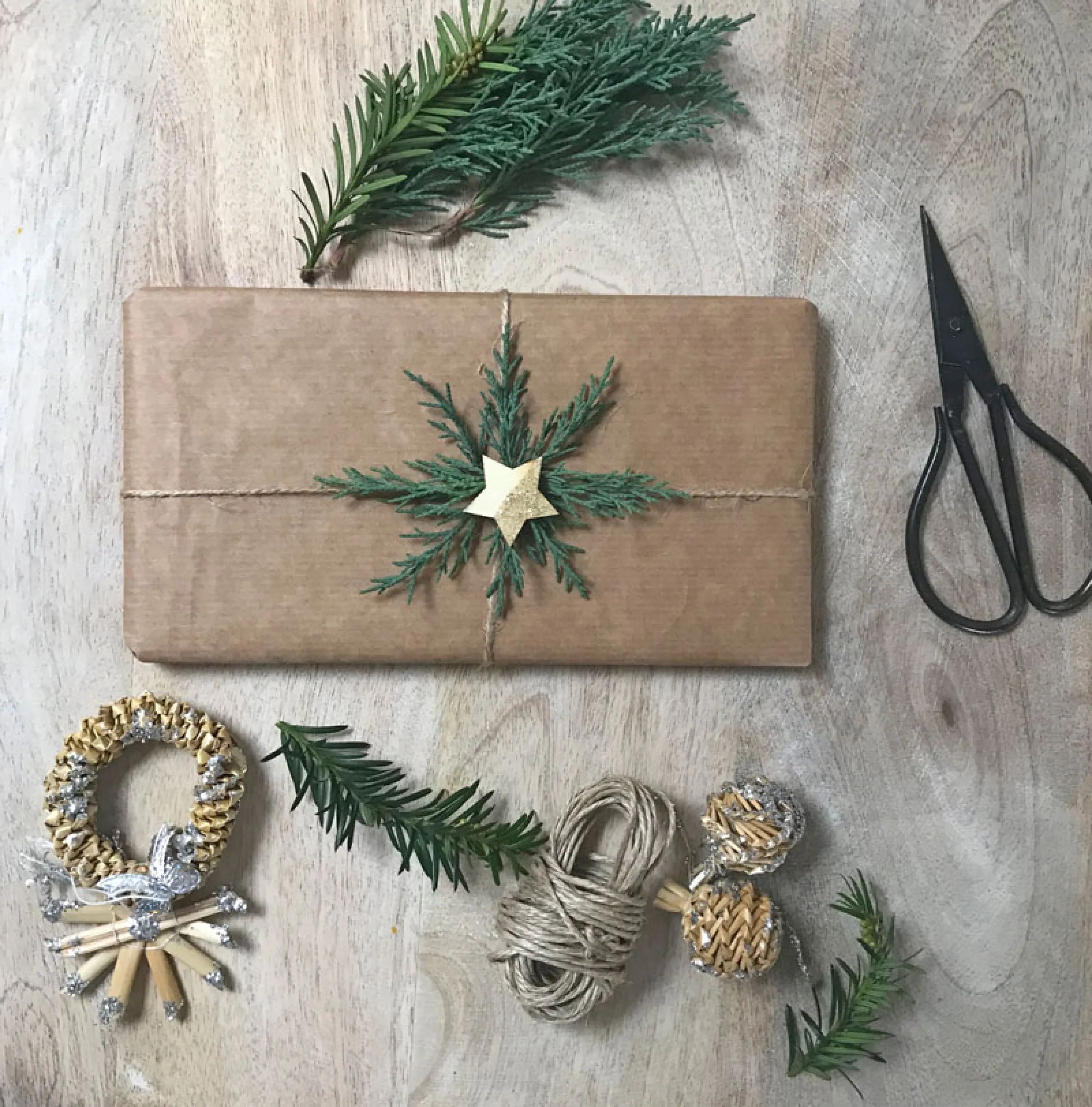 An example of sustainable Christmas gift wrapping where simple brown paper is decorated with some greenery twigs arranged radially and a golden star in the center.
